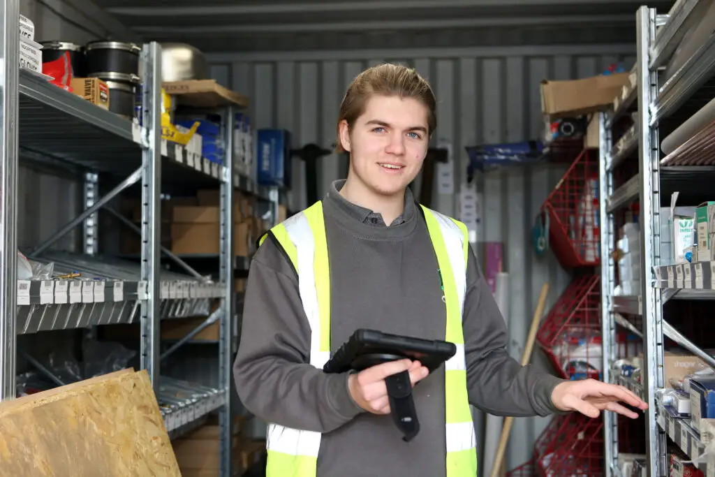 Young person in high visibility vest in a warehouse smiling at the camera