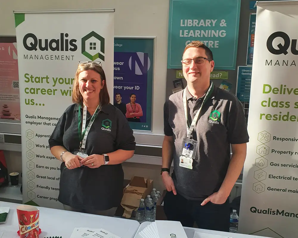 2 Qualis employees at a stall with Qualis branded roller banners behind them smiling at the camera