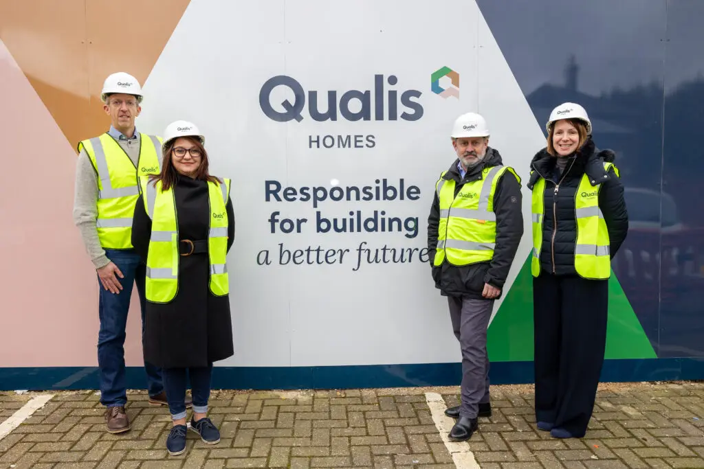 4 people in high visibility vests in front of Qualis Homes logo billboard