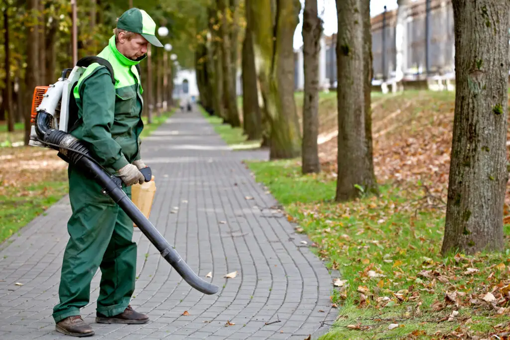 man in green uniform with leaf blower in park