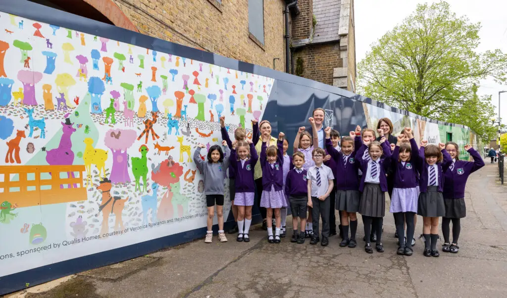 A group of school children in purple uniform cheering in front of a mural of art