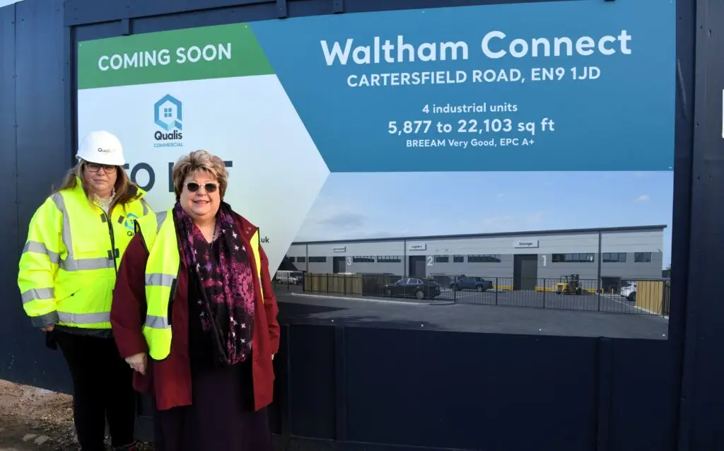 Two Women in high visibility vest smiling at the camera in front of a banner for Waltham Connect