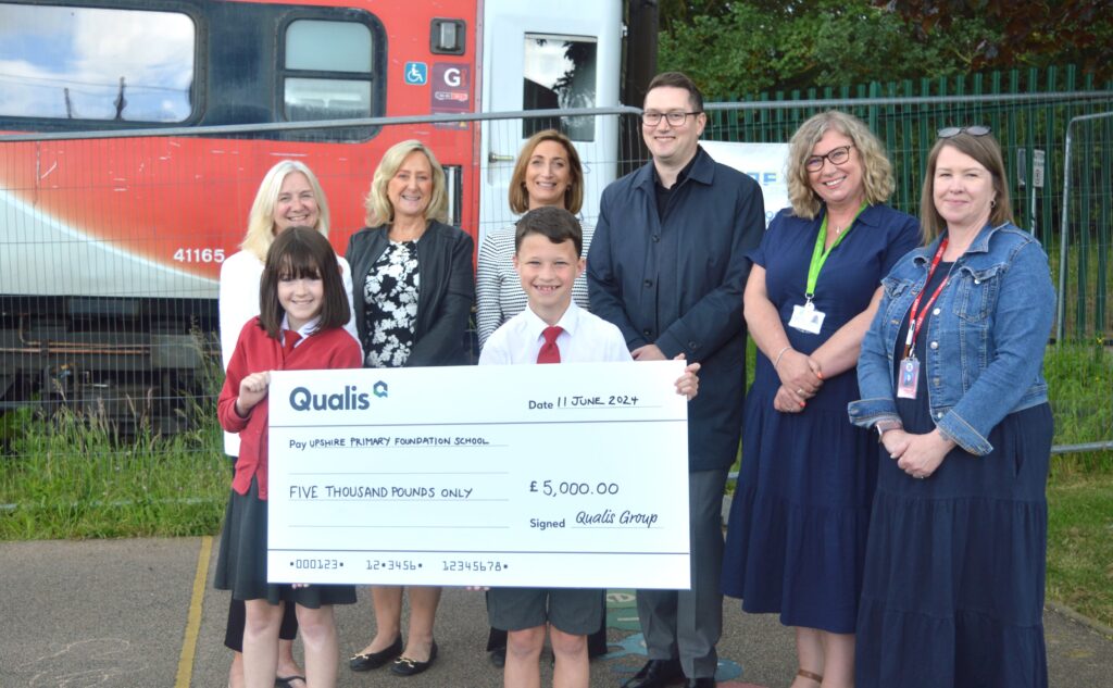 A group of six adults and two children stand in front of train carriage. The children hold a giant cheque.