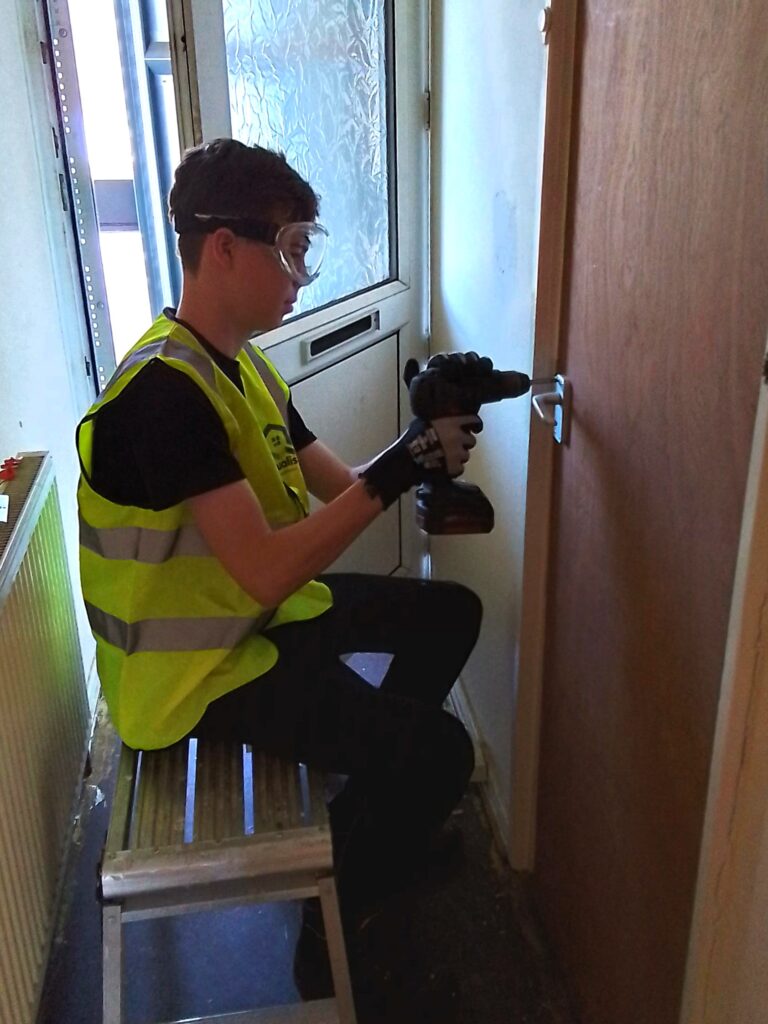 Photo of student in high vis workwear drilling a door handle