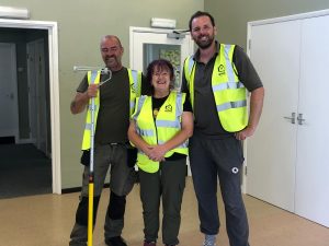 Two men stand either side of a woman all wearing Qualis high vis branded jackets. The man on the left carries a paint roller.