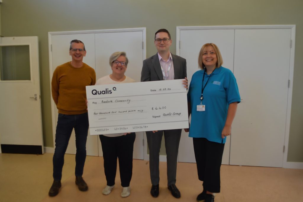 Four people stand holding a giant cheque made out to Restore Community from Qualis.