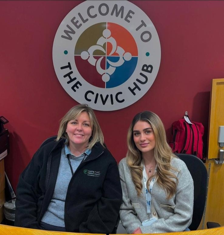 Two women sat behind a reception desk smile at the camera
