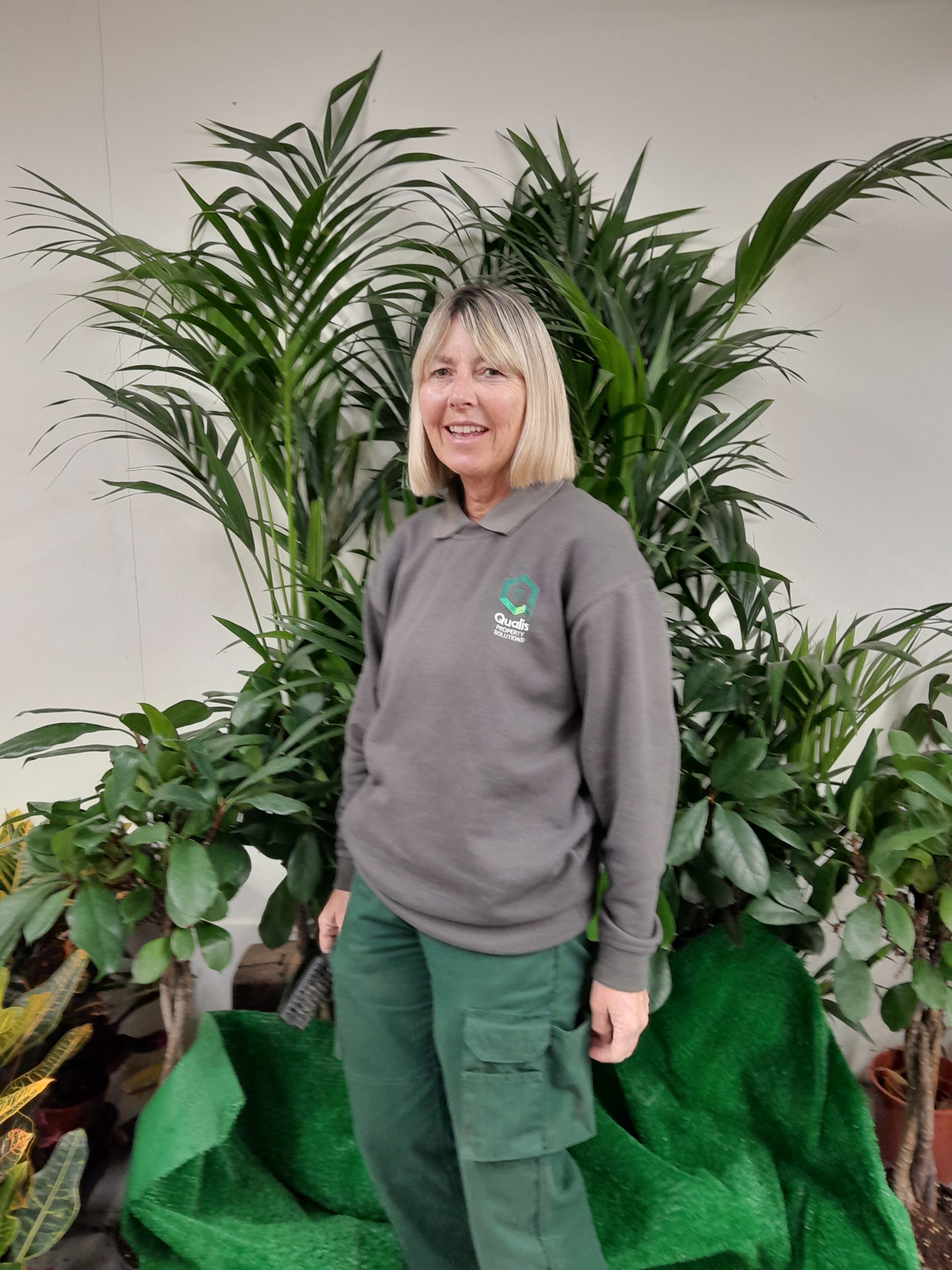 Blonde haired lady portrait standing in front of a large plant.