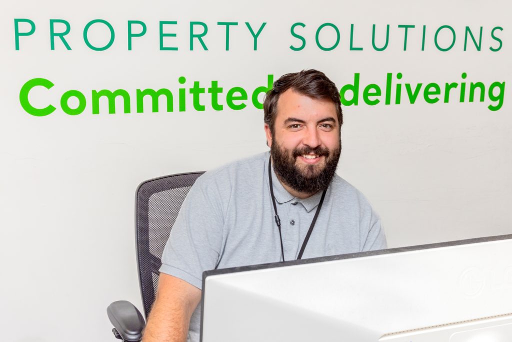 Man with beard sits behind a desk smiling at the camera