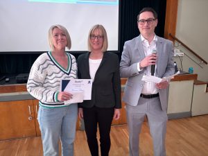 Woman holds certificate next to a woman and another man