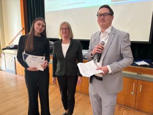 Woman holds certificate next to a woman and another man