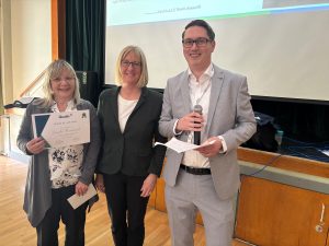 WoMan holds certificate next to a woman and another man