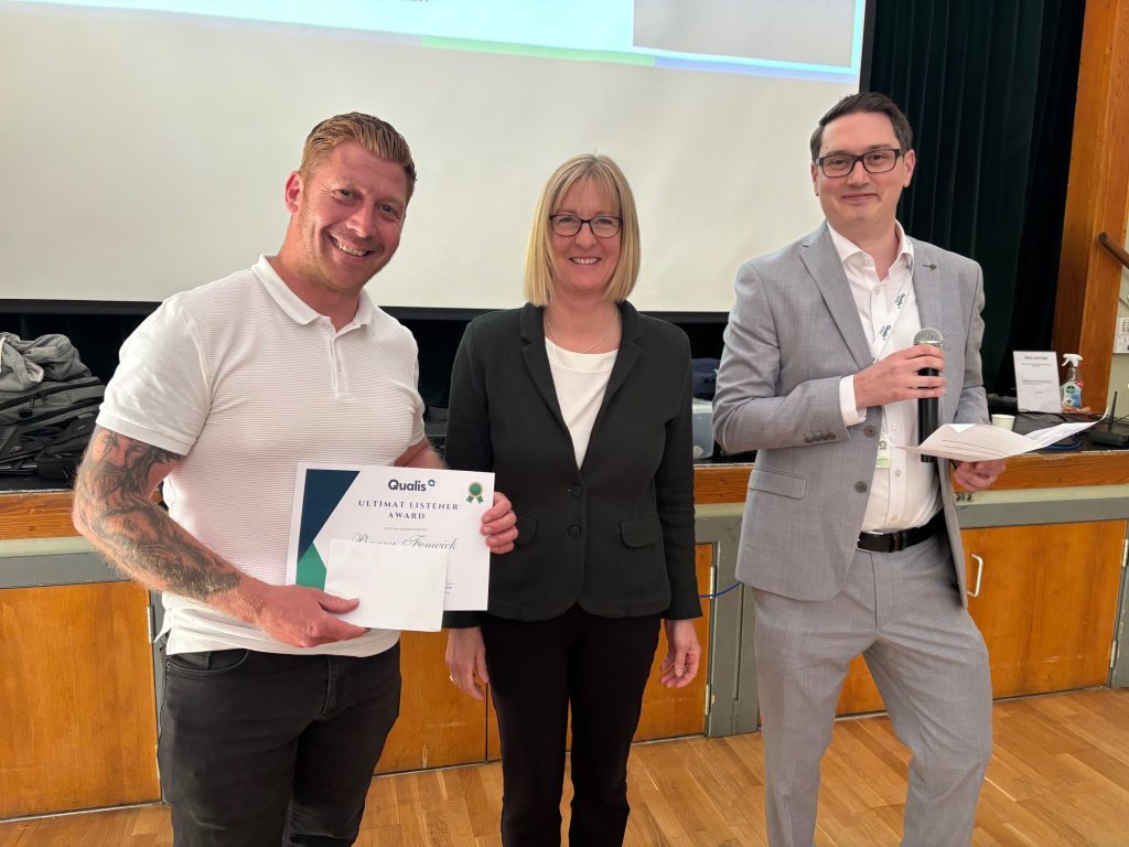 Man stands holding a certificate next to a woman and a man
