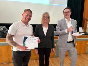 Man stands holding a certificate next to a woman and a man
