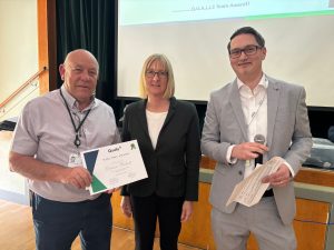 Man holds certificate next to a woman and another man