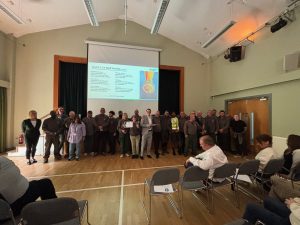 Team of app.30 men and women wearing work uniform stand in hall holding a certificate of award