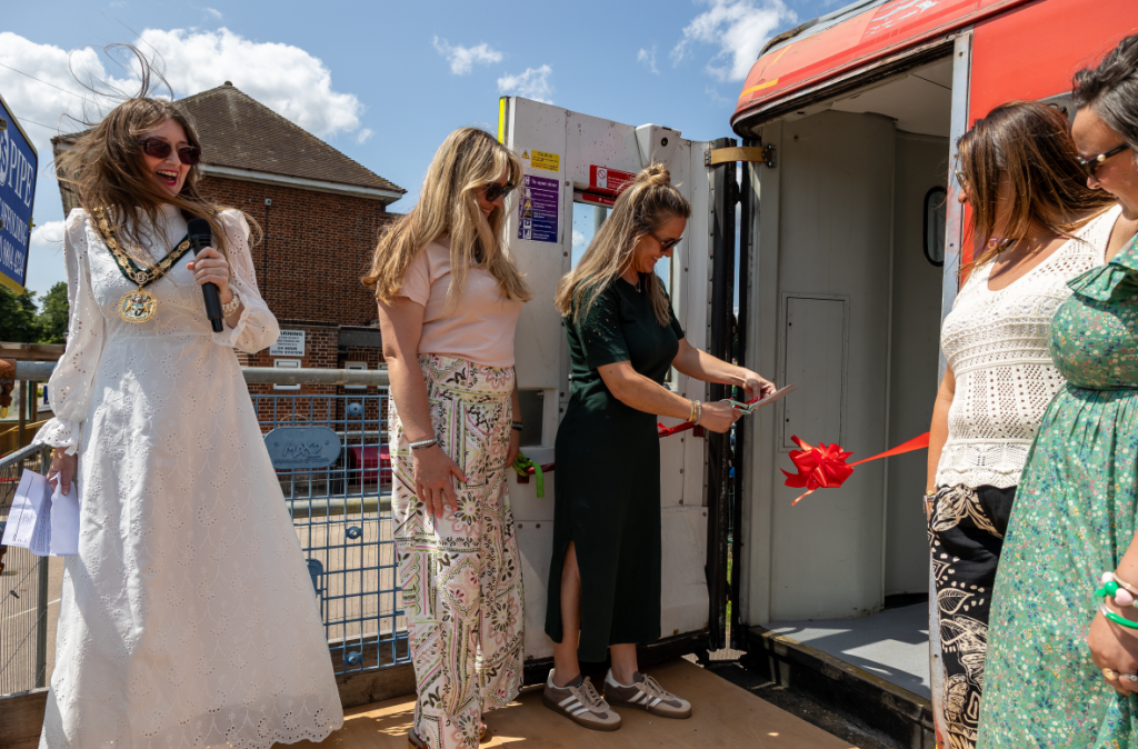 Five women stand at the entrance of a train carriage with one woman cutting a ribbon