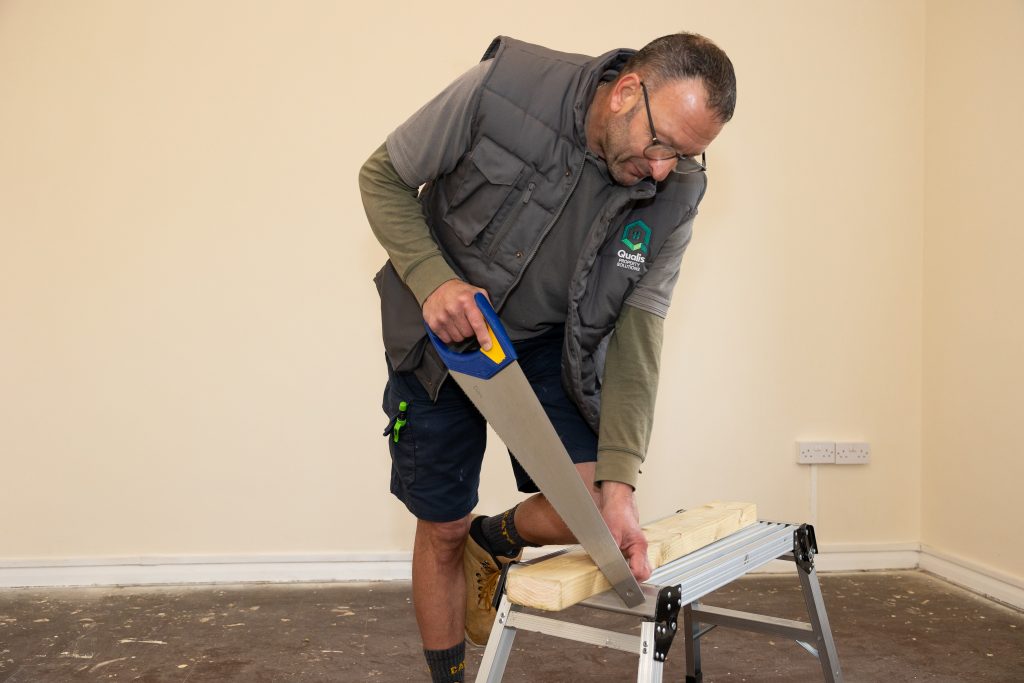 Qualis operative leans on a bench to saw a piece of wood