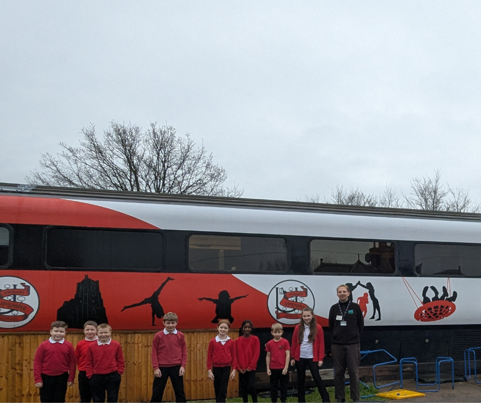 upshire primary school students and rocsteady msuci school teacher stand in front of the community train carriage