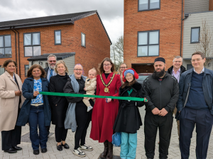 Chairman Louise Mead with her daughter Daisy,  alongside tenants of Milbourne Close, and EFDC CEO Andrew Small, Housing Director Dawn Harrisson, EFDC councillors Cllr Smruti Patel and Cllr Ray Balcombe, and Qualis' Ben Johnson, Sacha Jevans and Shanaz Begum cutting the ribbon to open the development.