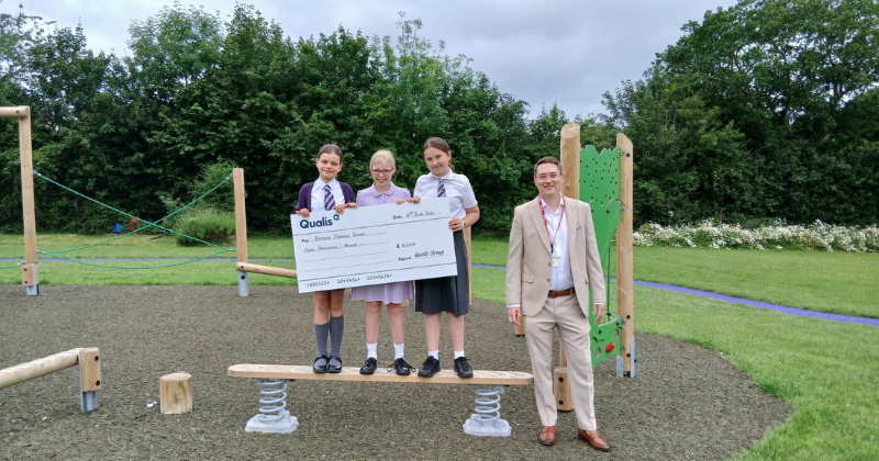 ben johnson from qualis stands with 3 school children who hold a large cheque